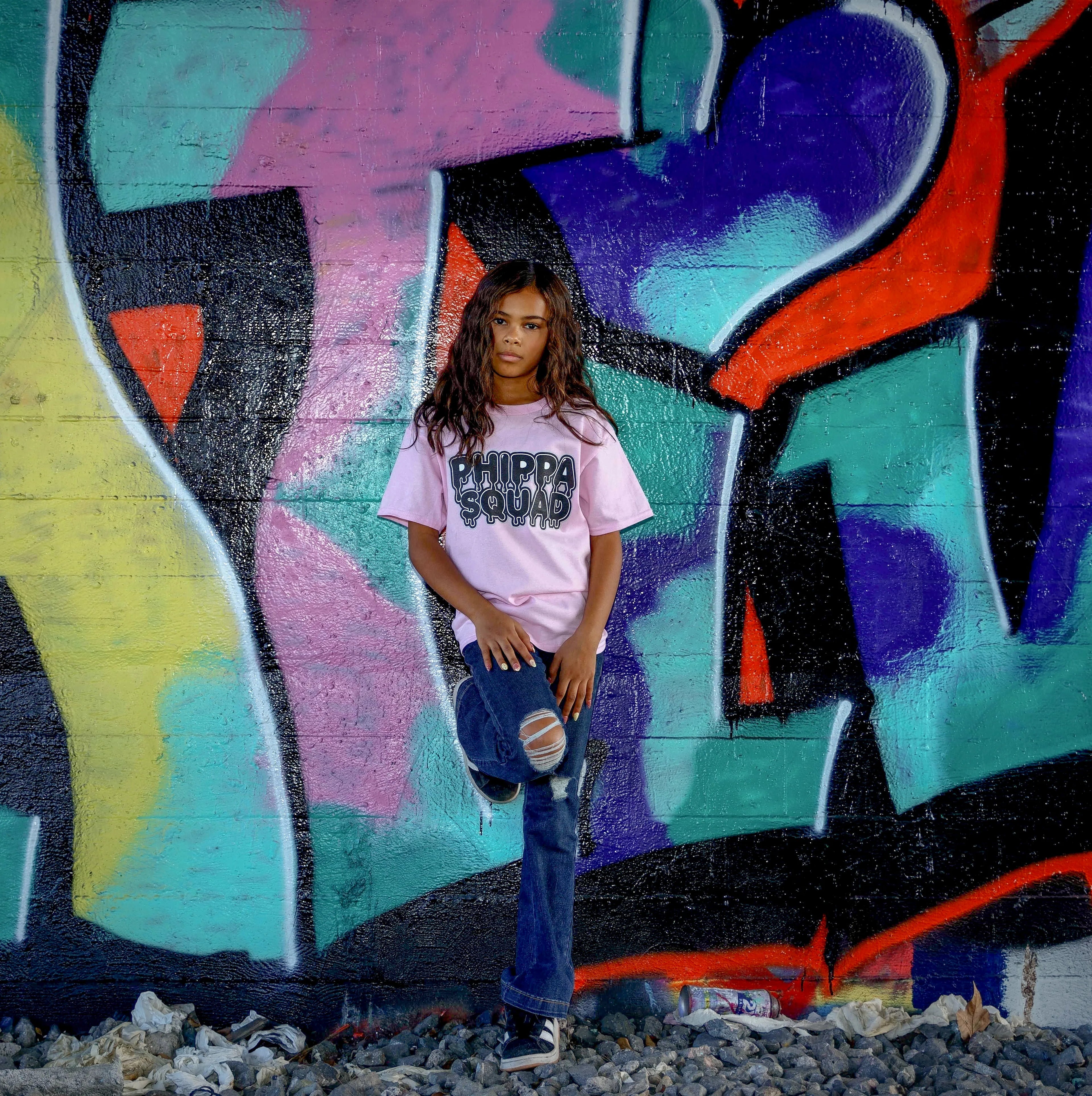 Girl wearing pink Phippa Squad tee in front of colorful graffiti wall - urban streetwear